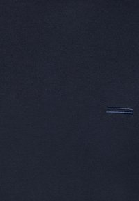 Marineblaue Baumwollbluse mit glatter Textur, die am Saum ein dezentes gestepptes Linienmuster für ein zusätzliches Designelement aufweist.