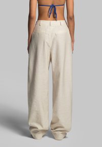 Cream-colored, wide-leg pants with a textured fabric, featuring a high waist and back pockets, seen from the rear.