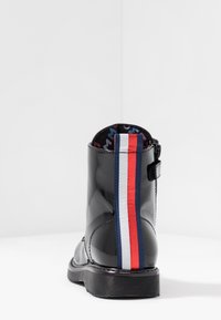 Černá kotníková bota z lakované kůže s kulatou špičkou, zdobená pruhovaným akcentem v červené, bílé a modré barvě na zadní straně a s texturovanou gumovou podrážkou.