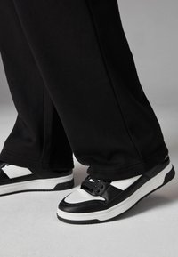 Black pants paired with black and white sneakers featuring a textured leather upper, white accents, and thick rubber soles.