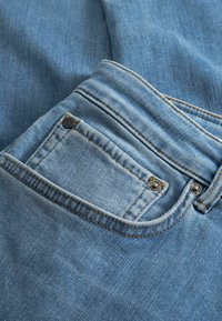 Lichtblauwe spijkerbroek met een achterzak, voorzien van koperen stiksel en metalen klinknagels. De stof heeft een zachte textuur met een verweerde finish.