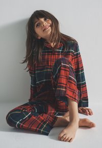 Set di pigiama a quadri rossi e verdi con colletto abbottonato, composto da maglia e pantaloni ampi, tessuto morbido e vestibilità comoda.