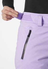 Fialové lyžařské kalhoty mají suchý zip, boční zipovou kapsu a elastický materiál. Pas je nastavitelný pro bezpečné uchycení.
