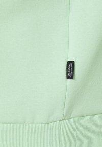 Sudadera verde claro con dobladillo y puños acanalados, con una pequeña etiqueta negra etiquetada "ONLY & SONS" en el lateral. Textura suave.