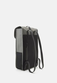 Zaino verticale in materiali grigi e neri con una finitura testurizzata. Dotato di spallacci regolabili e di una tasca laterale con zip. Design pulito e minimalista.