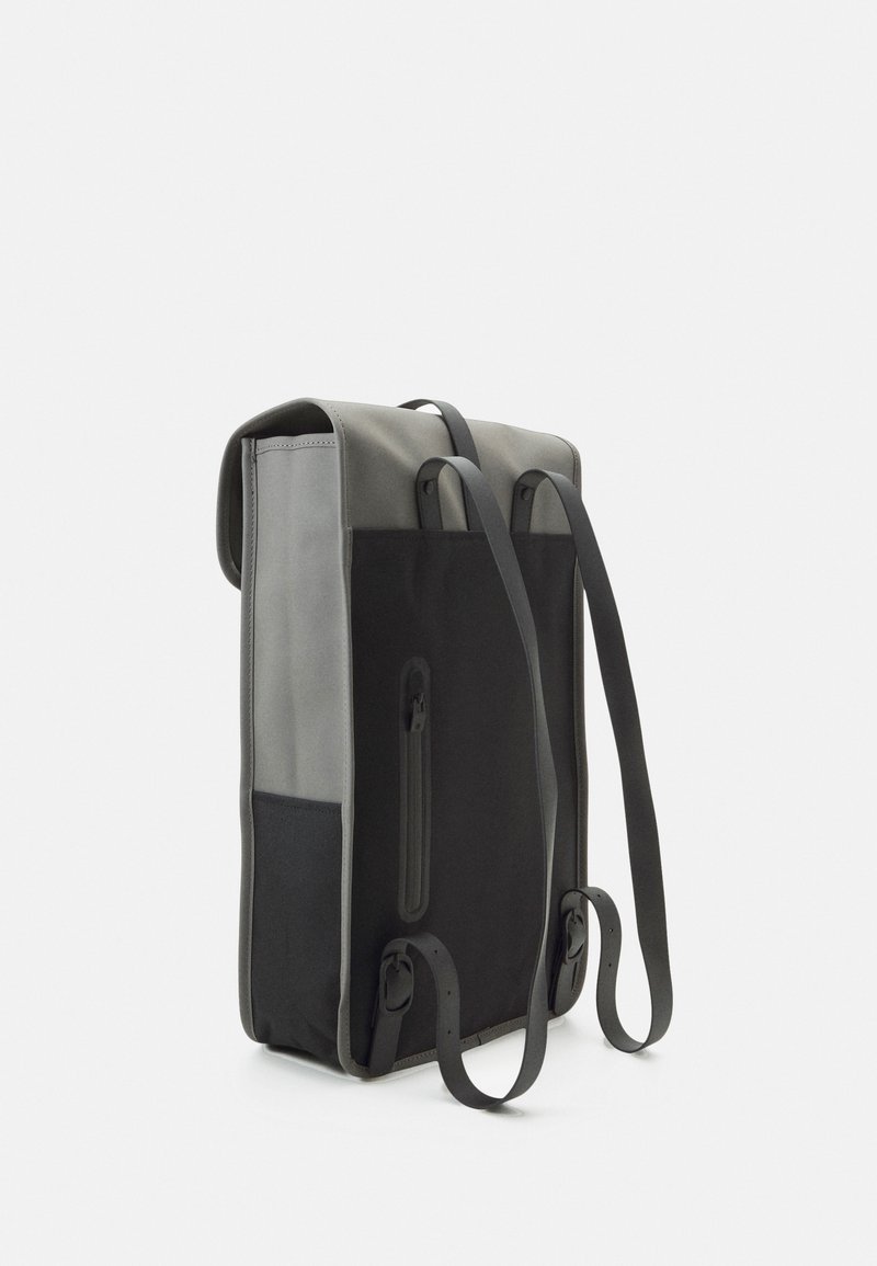 Sac à dos vertical en matériaux gris et noir avec une finition texturée. Dispose de bretelles ajustables et d'une poche zippée latérale. Design épuré et minimaliste.