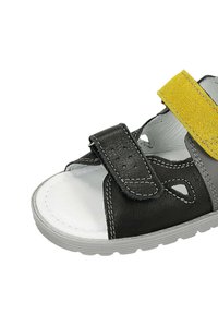 Sandalo nero e grigio con una fascia in suede gialla. Presenta una chiusura in Velcro regolabile, lati aperti e una suola testurizzata. Rivestimento interno morbido.
