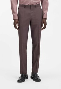 Braune maßgeschneiderte Hose mit subtil kariertem Muster, schlankem Schnitt, glatter Textur und einer Bügelfalte vorne, getragen mit schwarzen Schuhen.