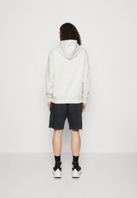 Felpa grigia chiara con cappuccio, abbinata a pantaloni cargo neri. L'outfit include sneakers alte nere con dettagli bianchi.