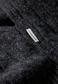 Donkergrijze gebreide sweaterstof, met een getextureerd oppervlak van zachte vezels, voorzien van een wit label met de tekst "LINDENBERGH" erop gedrukt.