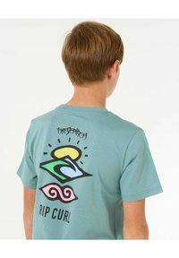 Camiseta de algodón verde menta con un gráfico colorido en la parte posterior que presenta diseños de sol, ola y remolino; texto "LA BÚSQUEDA" y "RIP CURL".