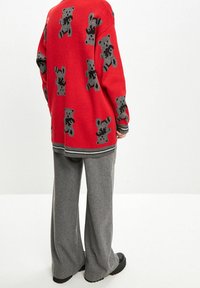 Maglione rosso con motivi di orsi grigi, maniche lunghe e orlo a righe, abbinato a pantaloni grigi larghi e scarpe nere.
