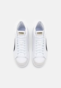 Paire de baskets montantes blanches Puma avec des rayures latérales noires, un logo doré sur la languette et des lacets blancs, vue de dessus sur un fond blanc.