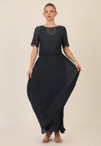 Zwart avondjurk met een kant bodice, korte mouwen, geplooide rok en ruches aan de onderrand. Glad materiaal met een vloeiende silhouet.