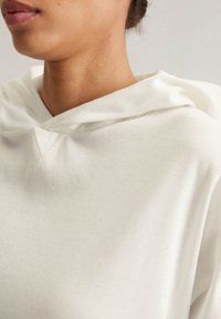 Felpa bianca in cotone con una texture a coste, dotata di cappuccio con cordini, cuciture a V sul collo e vestibilità comoda.