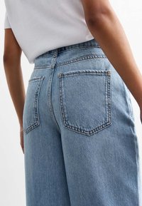 Light blue denim jeans with a loose fit, featuring two back pockets and visible stitching details. The fabric has a medium texture.