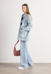 Veste en denim bleu clair avec poches, assortie à un jean large bleu clair et des baskets blanches. Un sac à bandoulière rose est porté en travers.