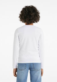 Weißes Langarmhemd aus glattem Stoff, mit Rundhalsausschnitt und schlichtem Design, kombiniert mit hellblauen Jeans.