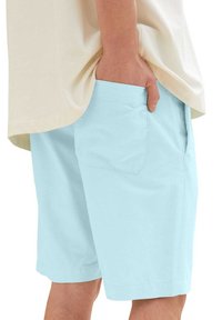 Light blue shorts made from fabric with a smooth texture. They feature side pockets and a straight cut, complemented by a pale shirt.