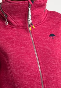 Fleece jacket in vibrant pink with a high collar, front zipper, and decorative umbrella logo. Features textured fabric and colorful zipper accents.