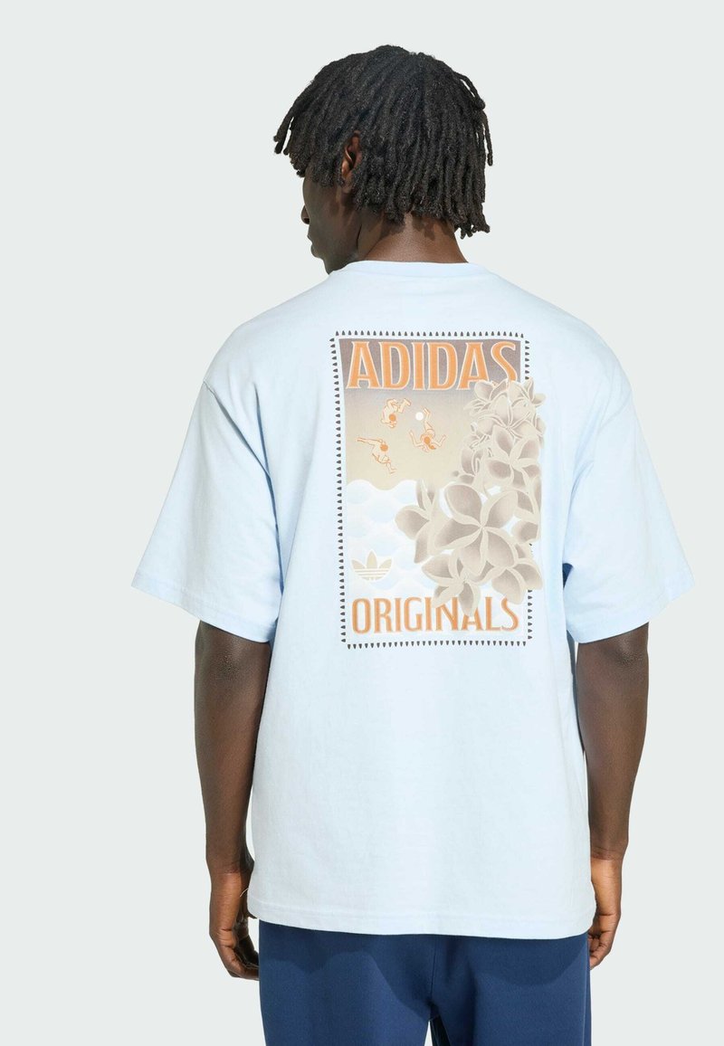 Mand iført lyseblå Adidas Originals T-shirt med blomster- og svømme-motiv på ryggen, set bagfra mod en ensfarvet baggrund.