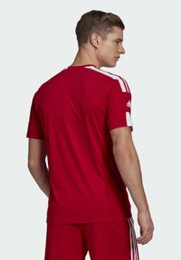 Maglia sportiva rossa con strisce bianche sulle spalle, maniche corte e scollatura tonda. Realizzata in materiale leggero e traspirante.