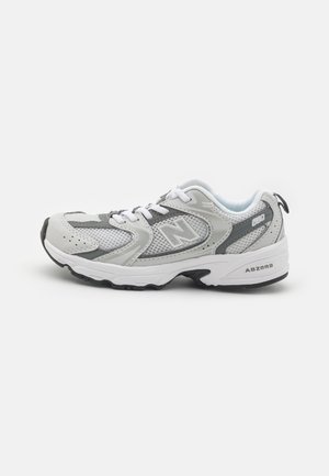 Szaro-białe buty do biegania New Balance z siatkową cholewką, sznurowadłami i teksturowaną gumową podeszwą, widok z boku na białym tle.