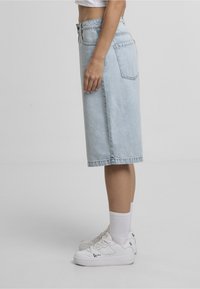 Lyseblå denim midinederdel med lige snit, lukning med knapper foran og to baglommer, kombineret med hvide sneakers og mellemlange sokker.
