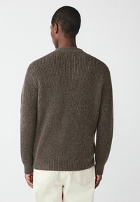 Brauner gerippter Pullover mit Rundhalsausschnitt und langen Ärmeln, der ein strukturiertes Strickmuster und einen taillierten Saum aufweist, von hinten gezeigt.