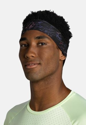 Joven con una cinta negra estampada en la cabeza y una camiseta deportiva transpirable de color verde claro, mirando ligeramente de lado con una expresión neutral.