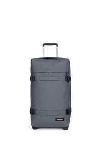 Sac à roulettes gris de forme rectangulaire, fabriqué en tissu durable. Il dispose d'une poignée télescopique, de boucles noires et d'un patch logo à l'avant.