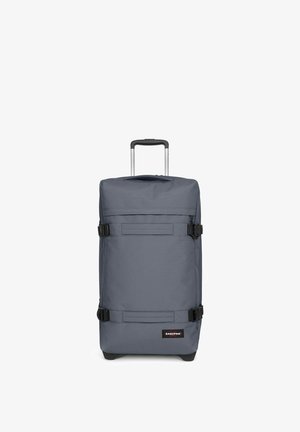 Sac à roulettes gris de forme rectangulaire, fabriqué en tissu durable. Il dispose d'une poignée télescopique, de boucles noires et d'un patch logo à l'avant.