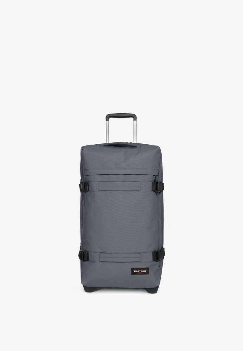 Sac à roulettes gris de forme rectangulaire, fabriqué en tissu durable. Il dispose d'une poignée télescopique, de boucles noires et d'un patch logo à l'avant.