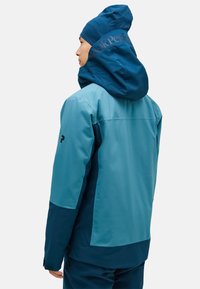 Blue and teal waterproof jacket with a large hood, featuring a logo on the back, and matching blue beanie. Smooth, durable fabric.