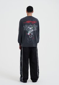 Dark grey long-sleeve shirt with a large skull and cross design on the back, paired with black wide-leg pants featuring side embellishments.