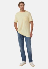 Lichtgele t-shirt met korte mouwen en een borstzak, gecombineerd met blauwe denim jeans en witte sneakers met beige zolen.