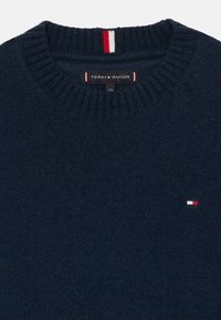 Námornícky pletený sveter s rebrovaným okrúhlym výstrihom, na hrudi má malé logo Tommy Hilfiger v červenej, bielej a modrej farbe.