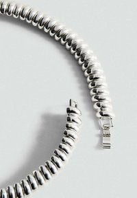 Segment d'un collier en argent brillant enroulé avec un fermoir rectangulaire sur une surface gris clair.