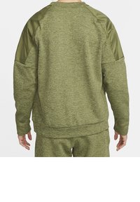 Personne portant un sweat texturé vert olive et un pantalon assorti, vue de dos sur un fond clair uni.