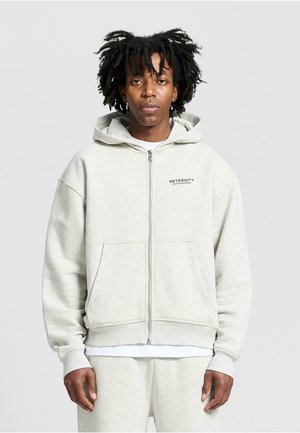 Light gray zip-up hoodie made of soft fabric, featuring a kangaroo pocket and ribbed cuffs. Includes logo text on the left chest.