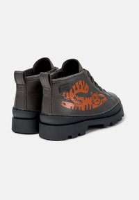 Scarpe in pelle grigia con una suola nera spessa, caratterizzate da design di zampe e facce di gatto arancioni sui lati. Stile low-top con lacci.
