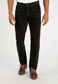 Pantaloni di velluto a coste verde scuro con vestibilità dritta, design a cinque tasche e chiusura con bottone, abbinati a scarpe marroni con lacci.