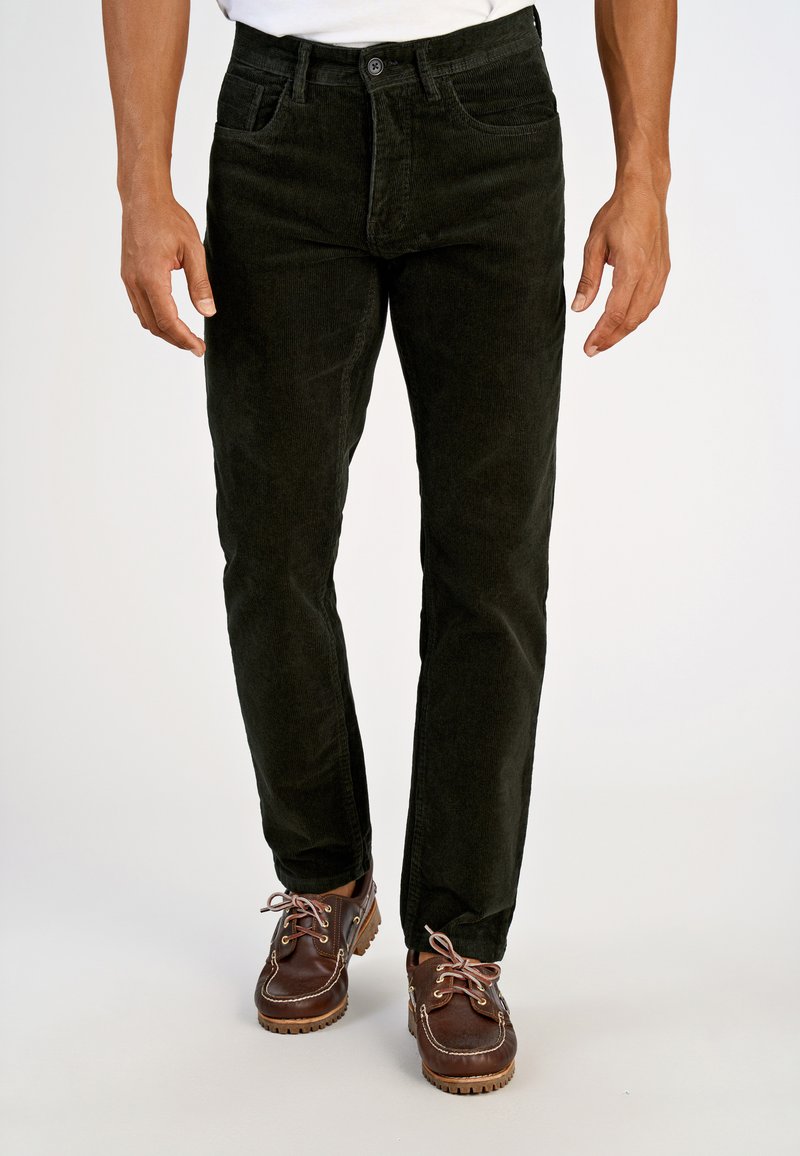 Pantaloni di velluto a coste verde scuro con vestibilità dritta, design a cinque tasche e chiusura con bottone, abbinati a scarpe marroni con lacci.