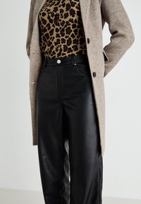 Manteau en laine brun mélangé porté sur un top à rayures imprimé léopard beige et un pantalon taille haute en simili cuir noir, avec des fermetures à bouton et à zip.