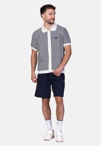 Kurzarm-Polohemd mit vertikalen Streifen in Marineblau und Weiß, Knopfverschluss und klassischem Kragen. Kombiniert mit marineblauen Shorts und weißen Turnschuhen.