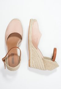 Wedge espadrilles featuring light pink suede upper, a braided jute heel, and a brown ankle strap. Rounded toe and smooth interior.