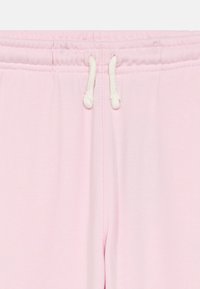 Svetlo roza trenirke z belo vrvico, zavezane na elastičnem pasu, gladka tekstura tkanine.