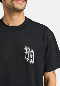 Czarny bawełniany t-shirt z okrągłym dekoltem i krótkimi rękawami. Zawiera biały graficzny logo na lewym piersi. Gładka tekstura.