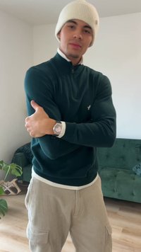 Žalias megztinis su užtrauktuku prie kaklo ir baltais akcentais, derinamas su smėlio spalvos kordurojos kelnėmis. Modelis dėvi baltą megztą kepurę ir sidabrinį laikrodį.