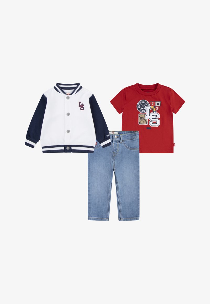 Piros póló nyomtatott grafikákkal, fehér és tengerészkék baseball dzseki gombokkal, valamint klasszikus szabású kék farmernadrág.